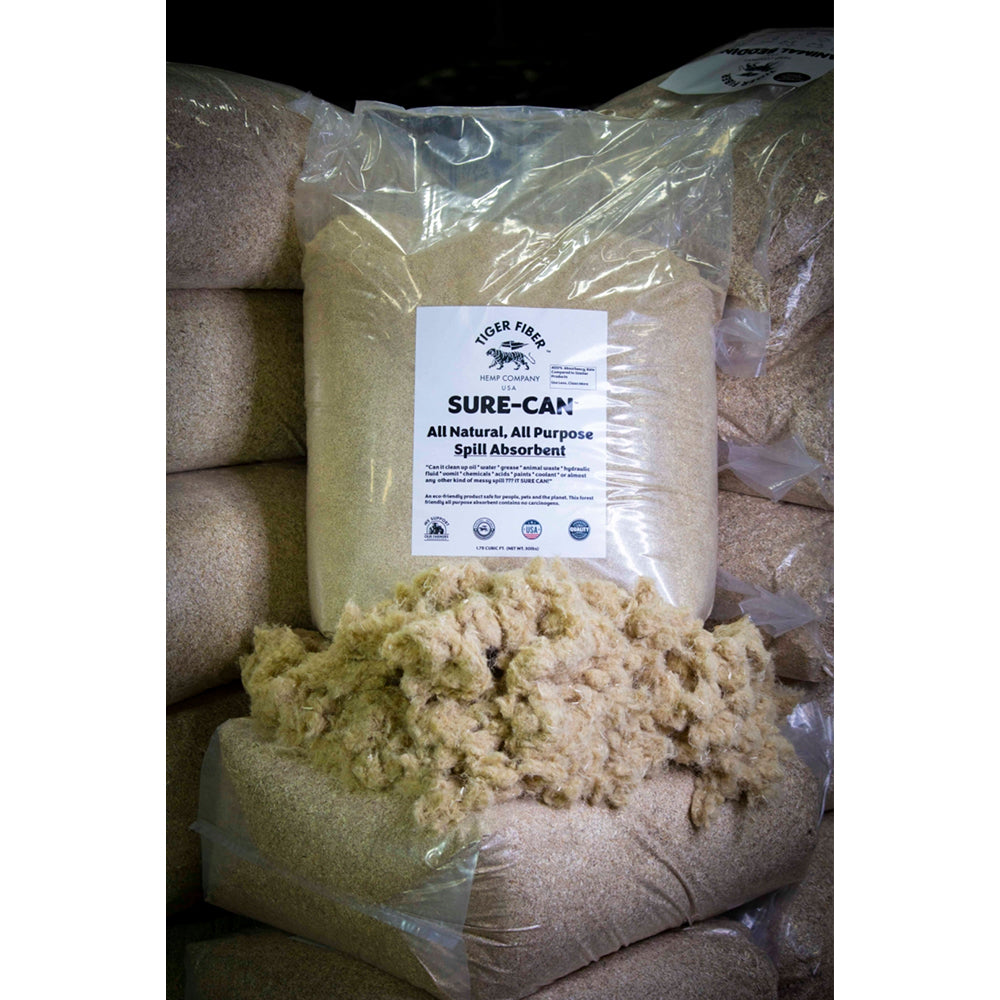 A 30 pound translucent packaged bag of hemp Sure-Can sits on top of raw hemp fiber in front of stacked piles of the same product displayed behind a pile of raw hemp fiber.